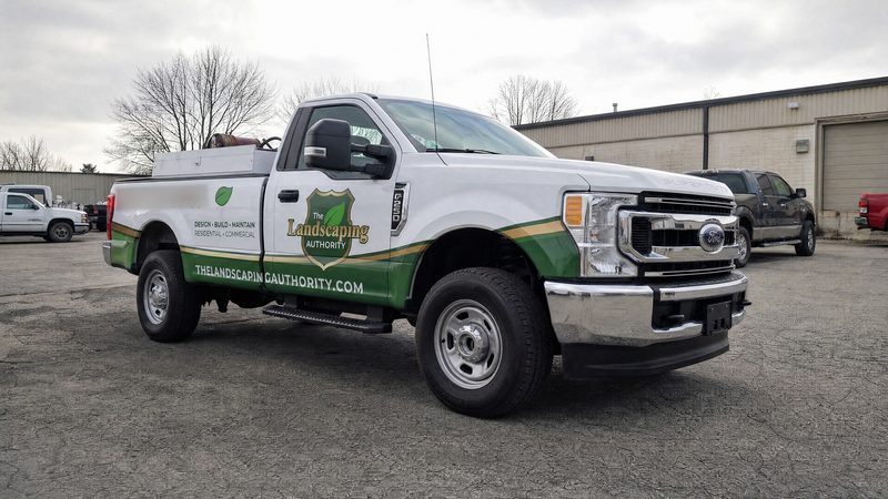 Concept mockup: white Ford F-250 pickup, low passenger-side front three-quarter view, showing the green hood-edge accent, the shield door logo, and the green and gold lower band.